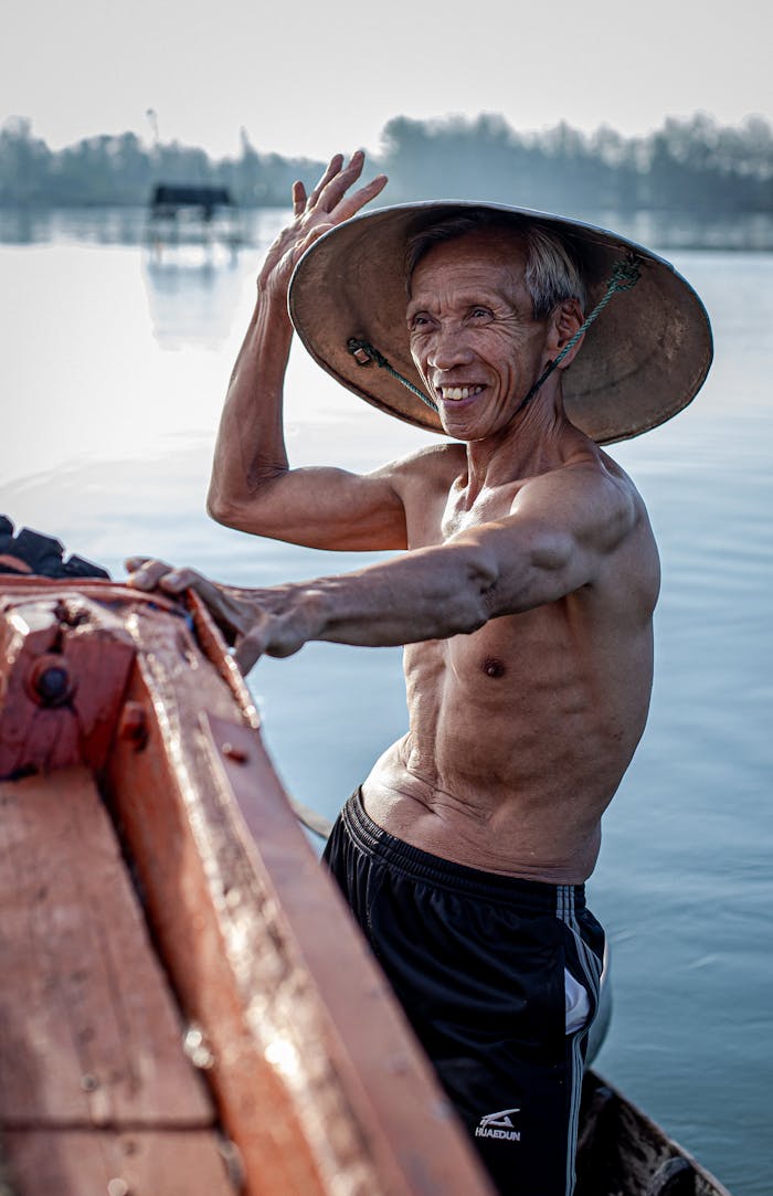 Elderly man wearing a conical hat smiling on a boat in Hội An, Vietnam.
